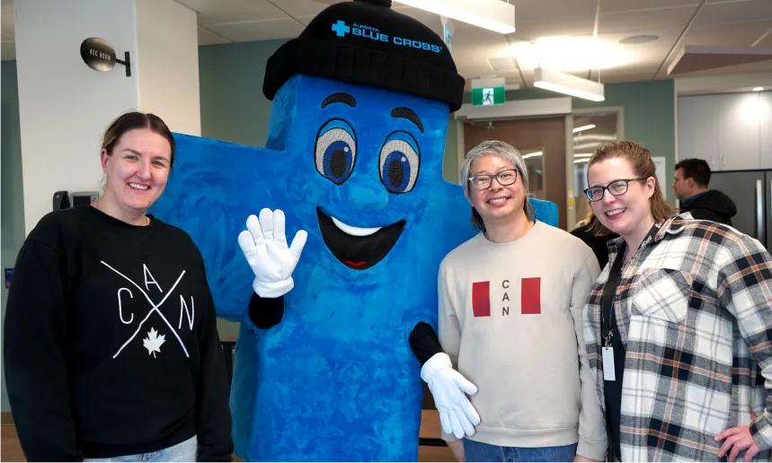 Three employees smiling while posing with a blue Alberta Blue Cross mascot.
