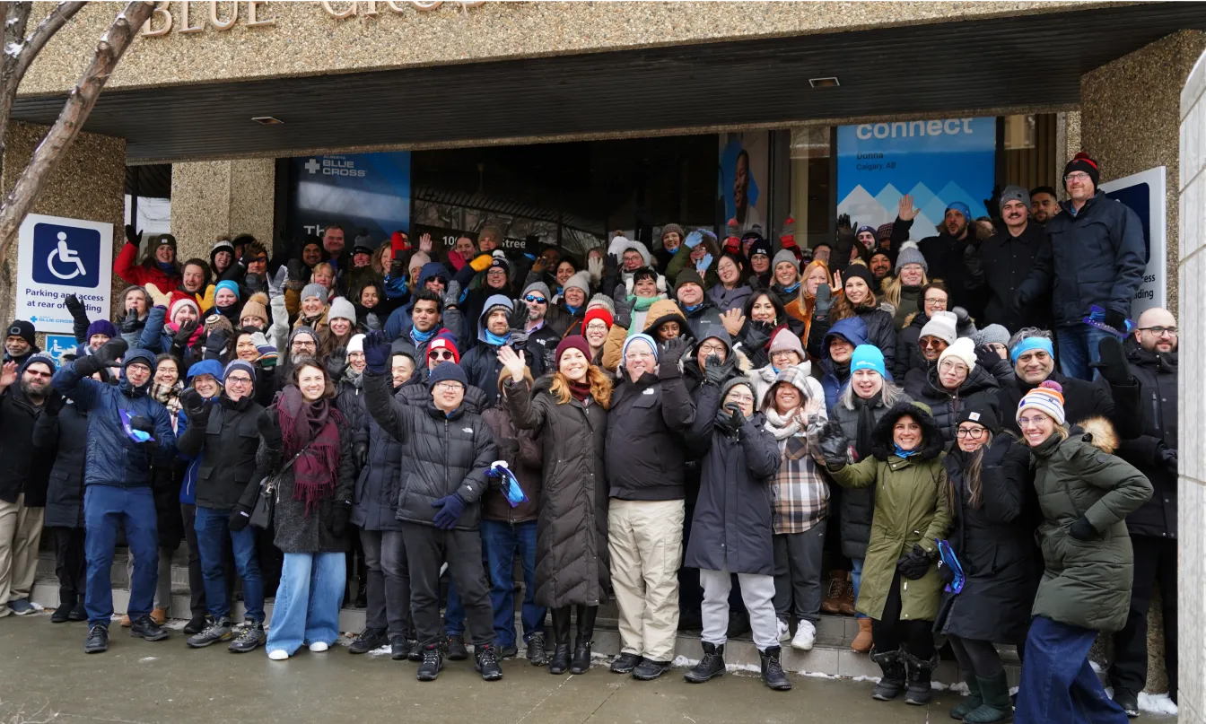 A large group of employees dressed for cold weather standing on the steps outside of the Alberta Blue Cross office building.